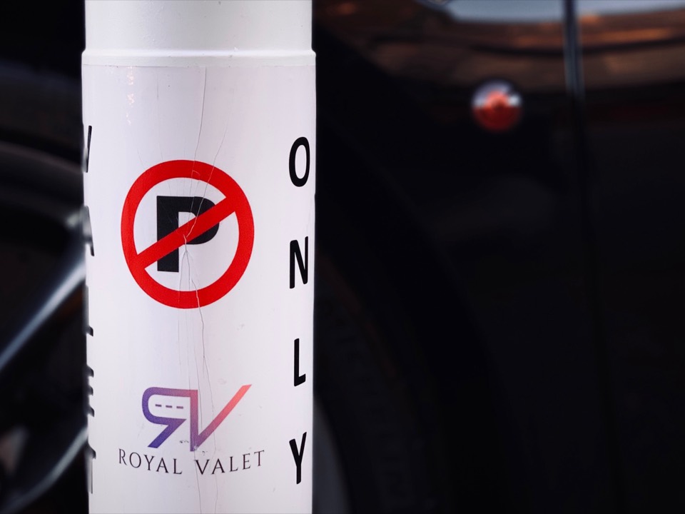 A Royal Valet sign at a valet-only stand in front of a parked Ferrari