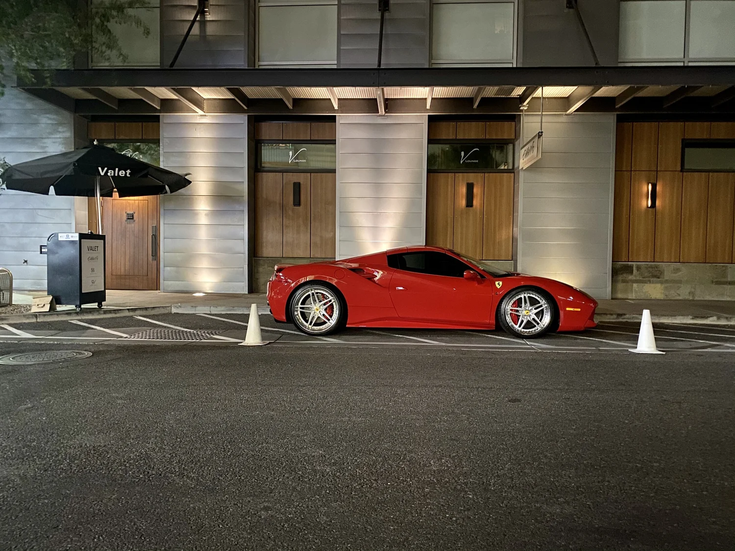 A red Ferrari parked at a Royal Valet stand at night
