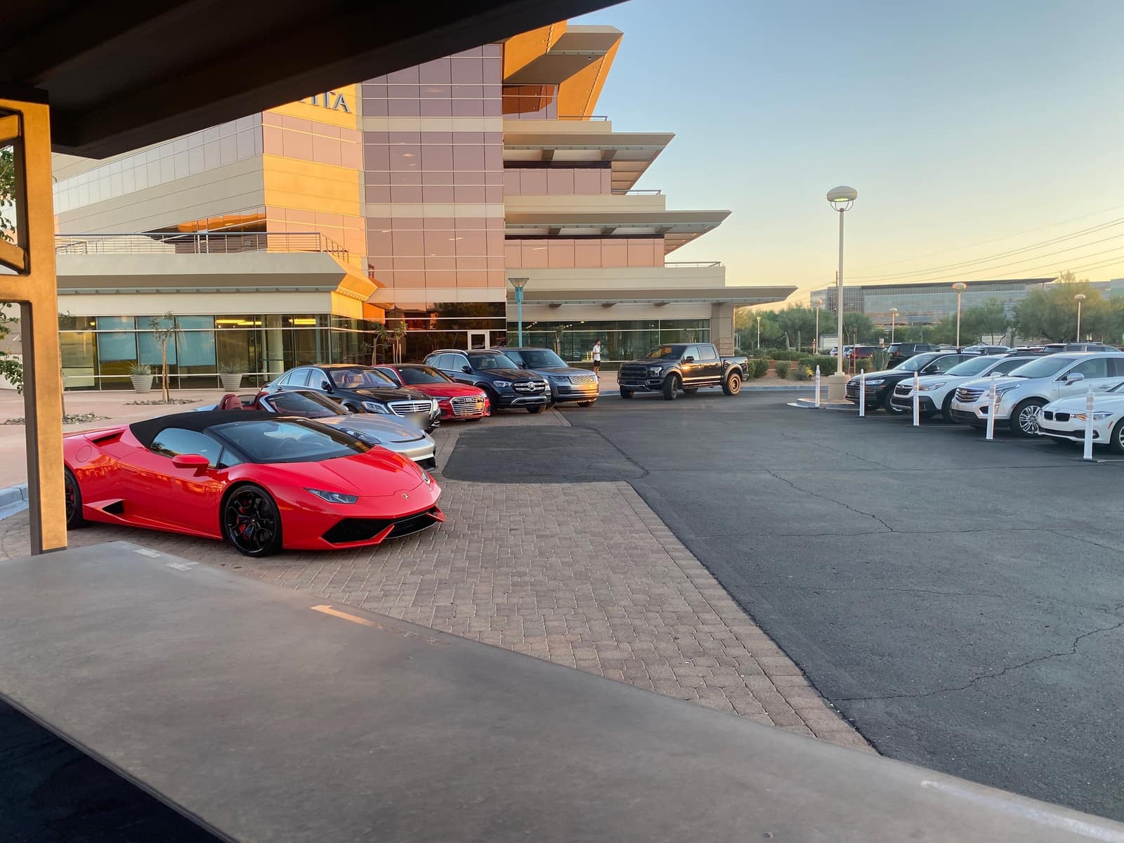 A red Lamborghini and a row of guests’ cars staged at a corporate campus at sunset